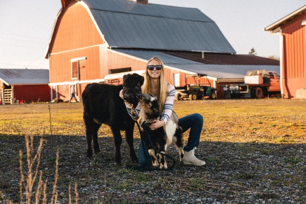 Pasture & Paw founder with Dexter calf and goat in front of the red farm barn